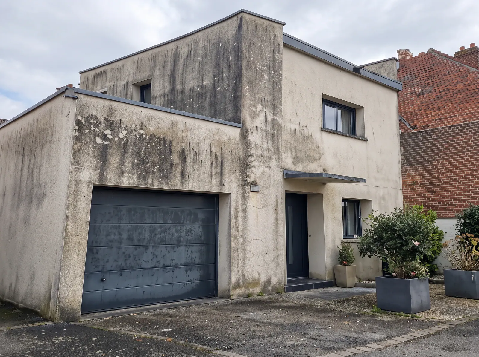 Façade dégradée d'une maison moderne à Isques avec traces d'humidité et algues vertes