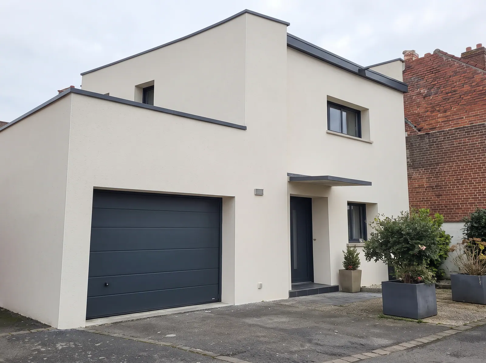 Maison moderne avec façade enduite blanche et garage gris foncé à Isques